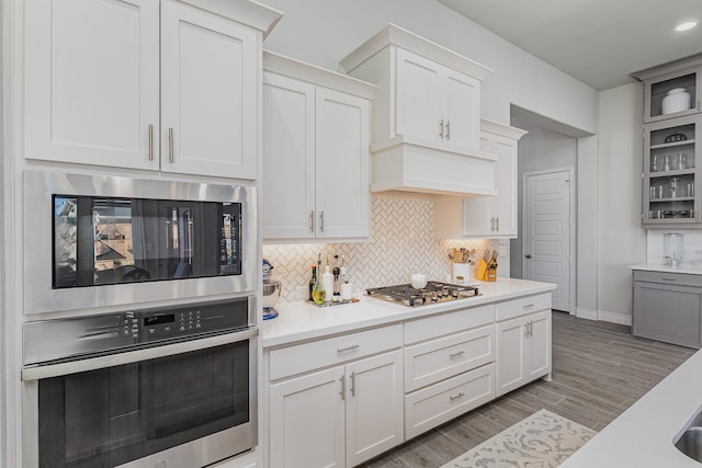 kitchen with dark wood-type flooring, appliances with stainless steel finishes, tasteful backsplash, white cabinetry, and custom range hood