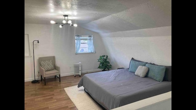 bedroom with radiator heating unit, a notable chandelier, a textured ceiling, vaulted ceiling, and hardwood / wood-style flooring