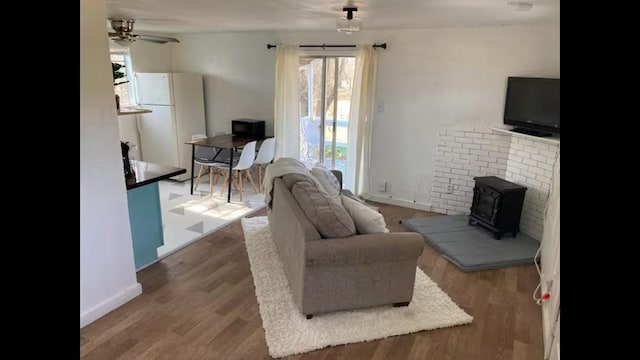 living room featuring wood-type flooring, a wood stove, and ceiling fan