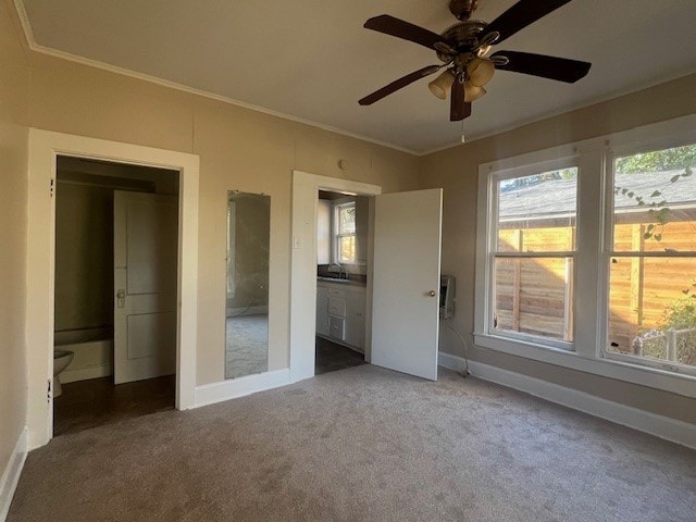 unfurnished bedroom with multiple windows, dark colored carpet, sink, and crown molding