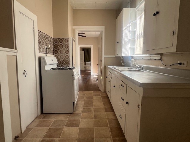 kitchen featuring dark tile patterned floors, sink, white gas stove, and white cabinets