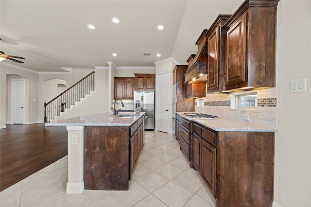 kitchen with a center island with sink, light hardwood / wood-style flooring, ornamental molding, light stone counters, and stainless steel appliances