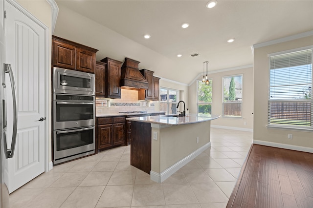 kitchen featuring premium range hood, crown molding, lofted ceiling, a kitchen island with sink, and light tile patterned flooring