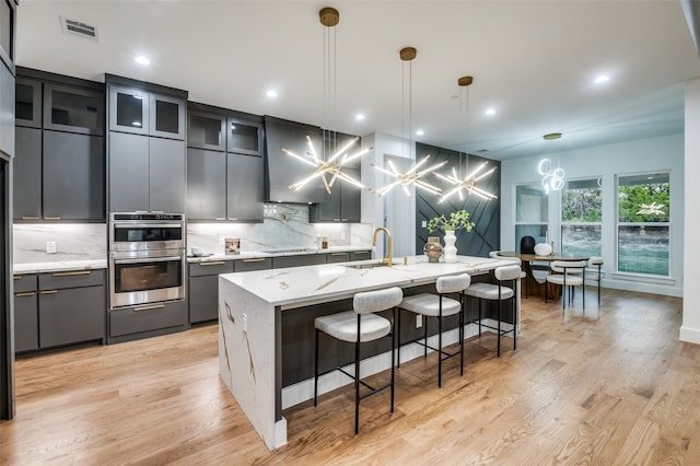 kitchen featuring decorative backsplash, pendant lighting, light wood-type flooring, and a center island with sink