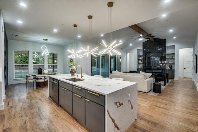 kitchen with light stone countertops, sink, vaulted ceiling with beams, a kitchen island with sink, and light wood-type flooring