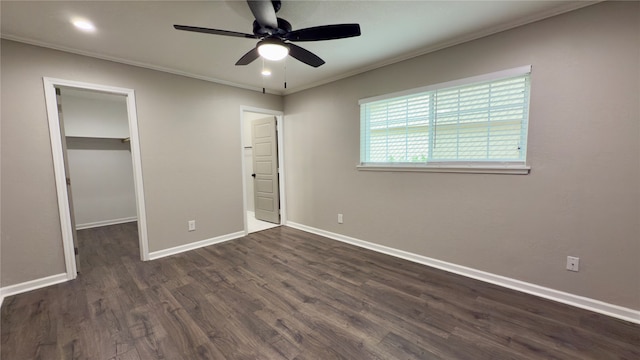 unfurnished bedroom featuring ceiling fan, crown molding, a walk in closet, a closet, and dark hardwood / wood-style flooring