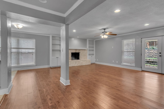 unfurnished living room with built in shelves, crown molding, a textured ceiling, light hardwood / wood-style floors, and ceiling fan