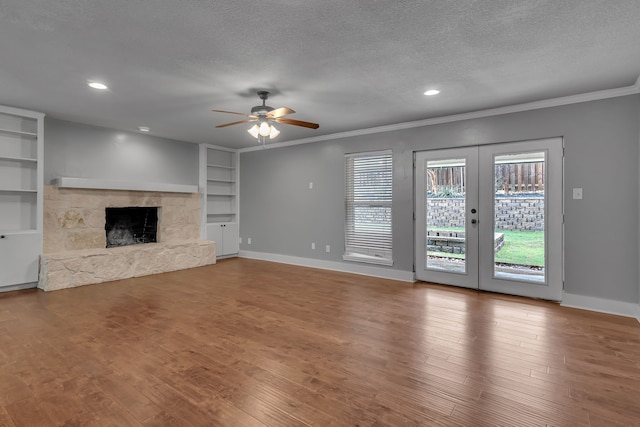 unfurnished living room featuring ceiling fan, a textured ceiling, hardwood / wood-style floors, a stone fireplace, and french doors