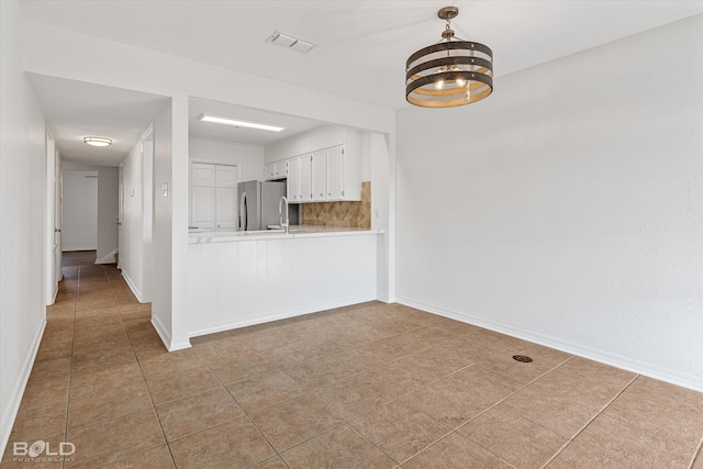 kitchen featuring white cabinets, kitchen peninsula, light tile patterned floors, a chandelier, and stainless steel fridge