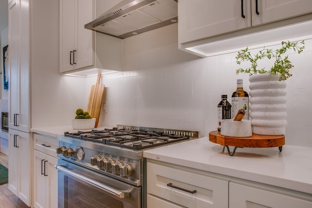 kitchen with white cabinets, high end stove, wall chimney exhaust hood, and wood-type flooring