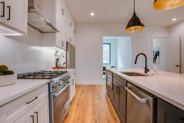 kitchen with light stone counters, stainless steel appliances, hanging light fixtures, white cabinets, and wall chimney exhaust hood