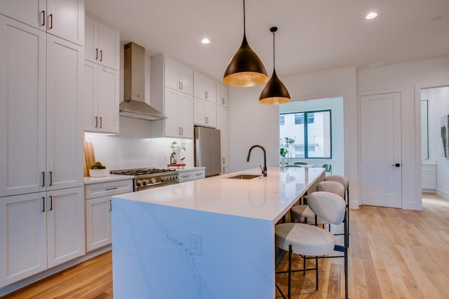 kitchen with stainless steel appliances, decorative light fixtures, sink, wall chimney exhaust hood, and light hardwood / wood-style flooring