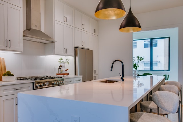 kitchen featuring stainless steel appliances, wall chimney exhaust hood, sink, an island with sink, and pendant lighting