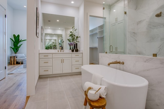 bathroom with wood-type flooring, vanity, separate shower and tub, and tile walls