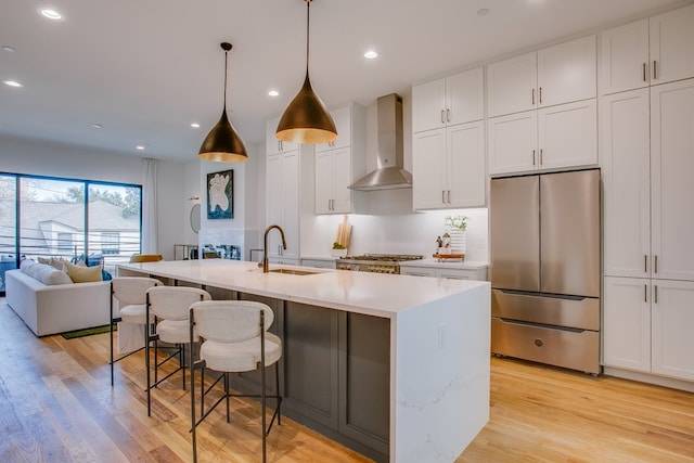 kitchen featuring wall chimney range hood, white cabinets, an island with sink, and stainless steel appliances