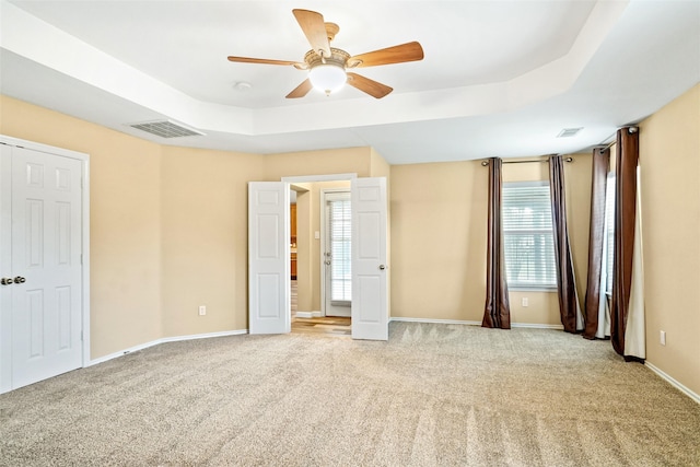 unfurnished bedroom with ceiling fan, a raised ceiling, and light colored carpet