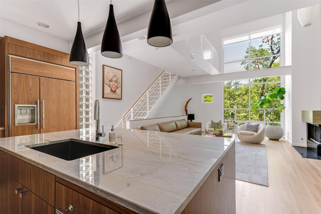 kitchen with light stone countertops, a towering ceiling, sink, light hardwood / wood-style flooring, and paneled built in fridge