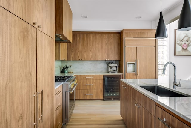 kitchen featuring high end appliances, sink, beverage cooler, decorative light fixtures, and light wood-type flooring