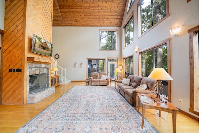 living room featuring wooden ceiling, high vaulted ceiling, a stone fireplace, wooden walls, and light wood-type flooring