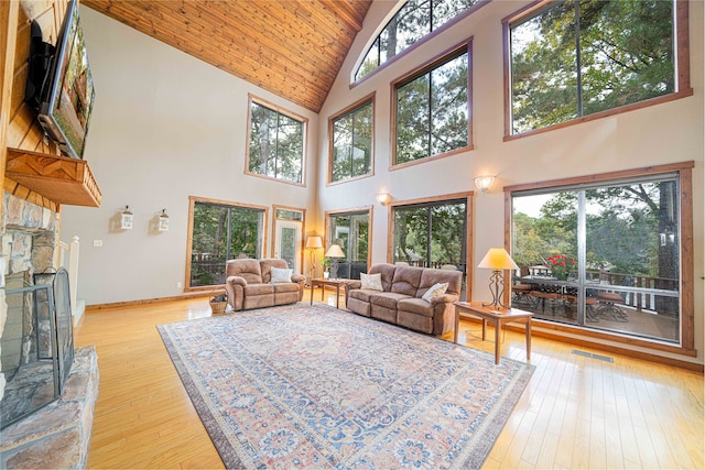 living room with high vaulted ceiling, a wealth of natural light, a stone fireplace, and light hardwood / wood-style flooring