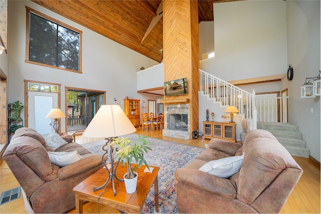 living room featuring a stone fireplace, light hardwood / wood-style floors, wooden ceiling, high vaulted ceiling, and beam ceiling