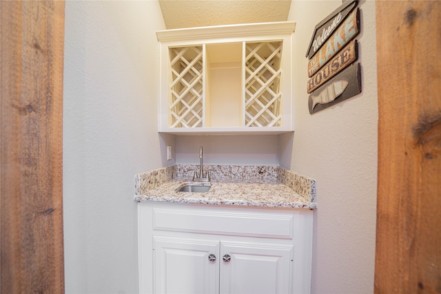 bar with white cabinets, sink, and light stone counters