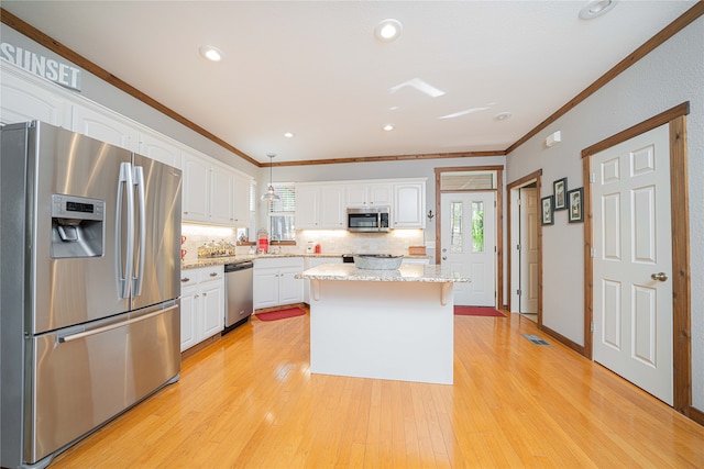 kitchen with appliances with stainless steel finishes, hanging light fixtures, light hardwood / wood-style flooring, a kitchen island, and white cabinets