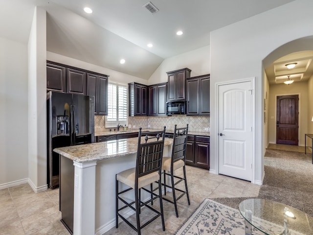 kitchen featuring lofted ceiling, light stone counters, a center island, black appliances, and dark brown cabinets