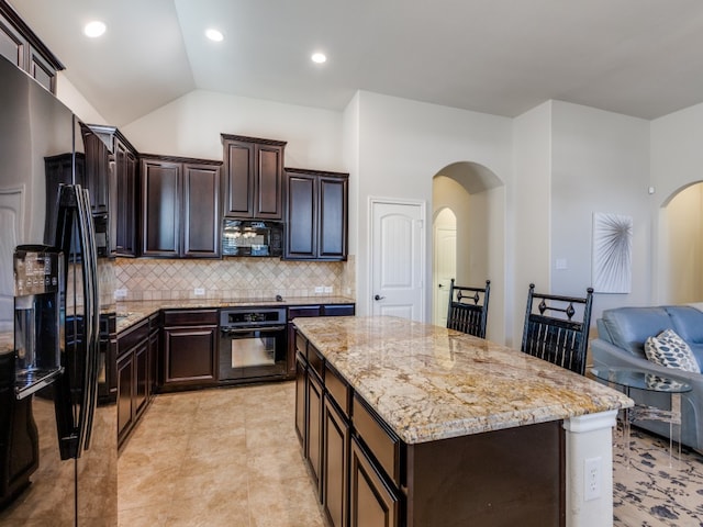 kitchen with black appliances, a kitchen island, backsplash, light stone countertops, and lofted ceiling