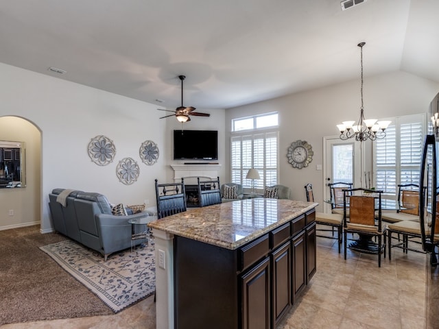 kitchen featuring light stone counters, ceiling fan with notable chandelier, a kitchen island, pendant lighting, and vaulted ceiling