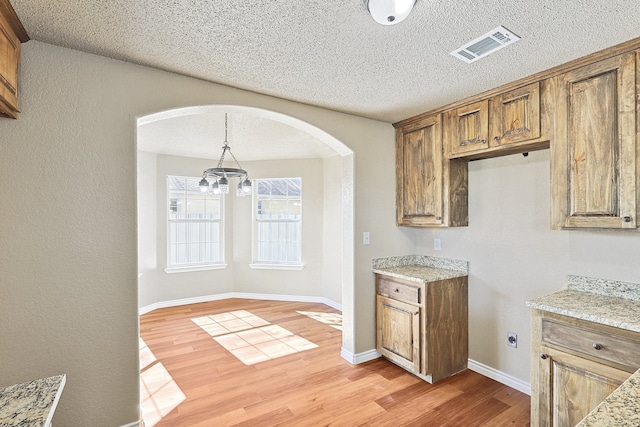 kitchen featuring a textured ceiling, visible vents, light wood finished floors, brown cabinetry, and pendant lighting