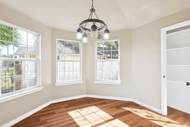 unfurnished dining area with a chandelier, a textured ceiling, baseboards, and wood finished floors