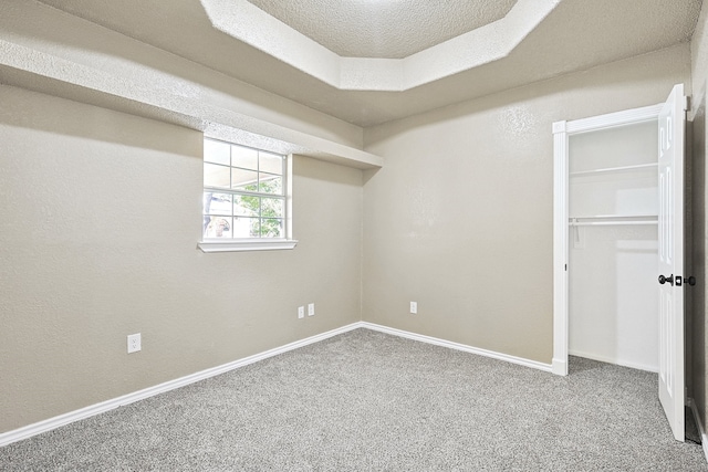 unfurnished bedroom featuring carpet floors, a closet, a raised ceiling, a textured ceiling, and baseboards