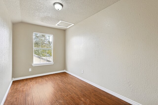 spare room featuring a textured ceiling, a textured wall, wood finished floors, and baseboards