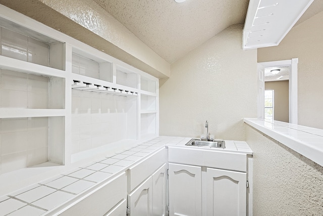 interior space with lofted ceiling, a textured ceiling, a sink, and a textured wall