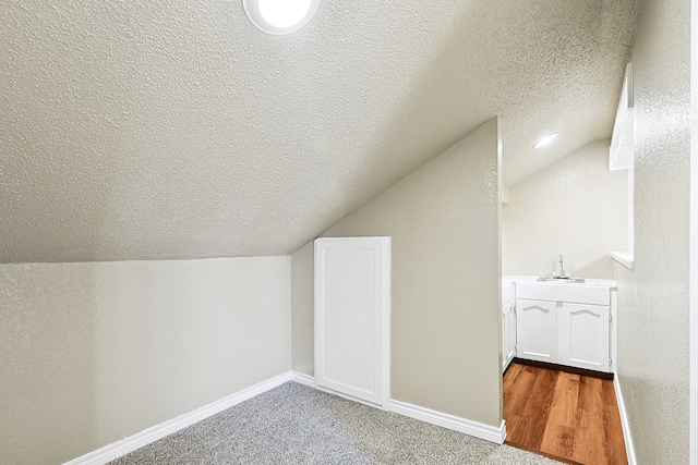 additional living space featuring baseboards, vaulted ceiling, and a textured ceiling