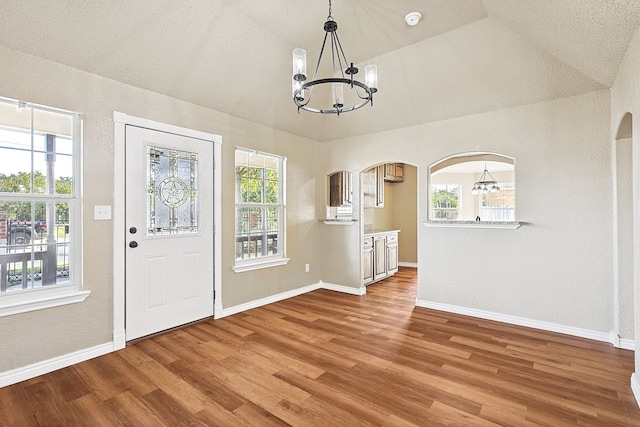 entryway with an inviting chandelier, lofted ceiling, and wood-type flooring