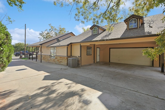 view of front of property with roof with shingles, central air condition unit, concrete driveway, an attached garage, and stone siding