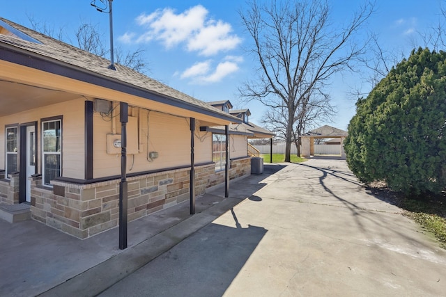 view of side of property with stone siding, a patio area, and fence