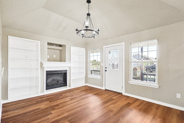 unfurnished living room featuring baseboards, built in features, wood finished floors, a textured ceiling, and a fireplace