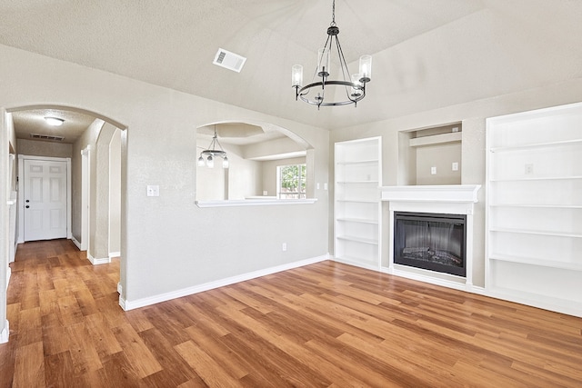 unfurnished living room with arched walkways, visible vents, baseboards, and wood finished floors