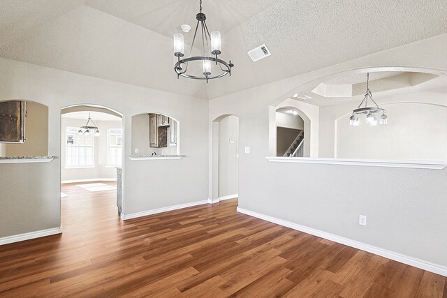 empty room with a chandelier, wood finished floors, arched walkways, and visible vents