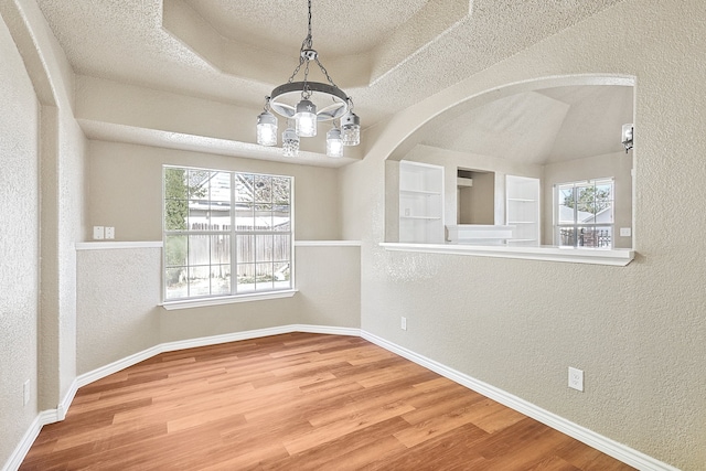 spare room featuring a textured wall, a textured ceiling, baseboards, and wood finished floors