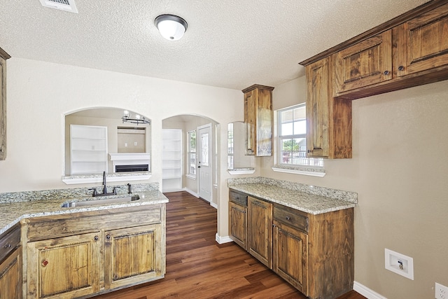 kitchen featuring dark wood-type flooring, a sink, a textured ceiling, and light stone counters