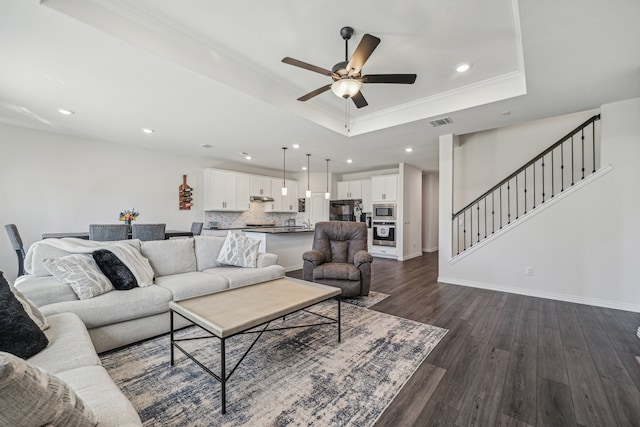 living room featuring dark wood-type flooring, crown molding, ceiling fan, and a raised ceiling