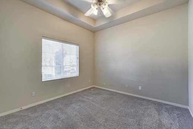 empty room featuring ceiling fan, a raised ceiling, and carpet floors