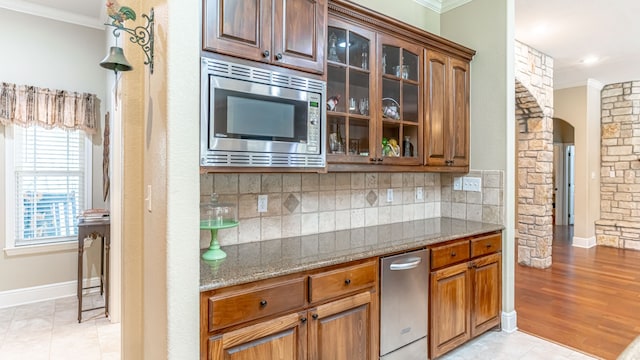 kitchen featuring light stone counters, tasteful backsplash, light hardwood / wood-style flooring, crown molding, and stainless steel microwave