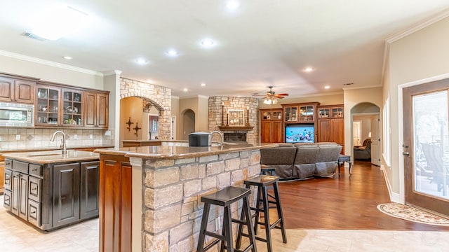 kitchen with a center island with sink, stainless steel microwave, ornamental molding, a breakfast bar, and light hardwood / wood-style flooring