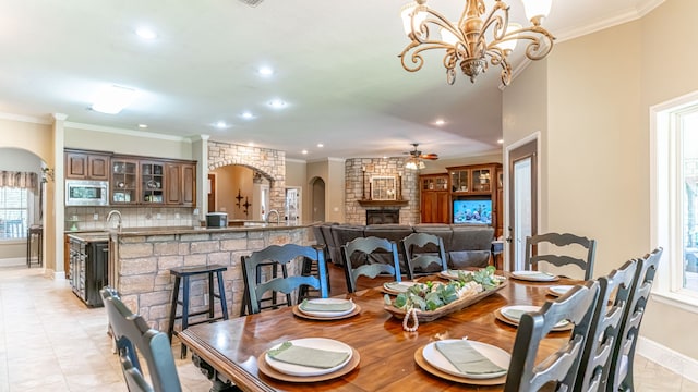 tiled dining room featuring a fireplace, ceiling fan with notable chandelier, and crown molding