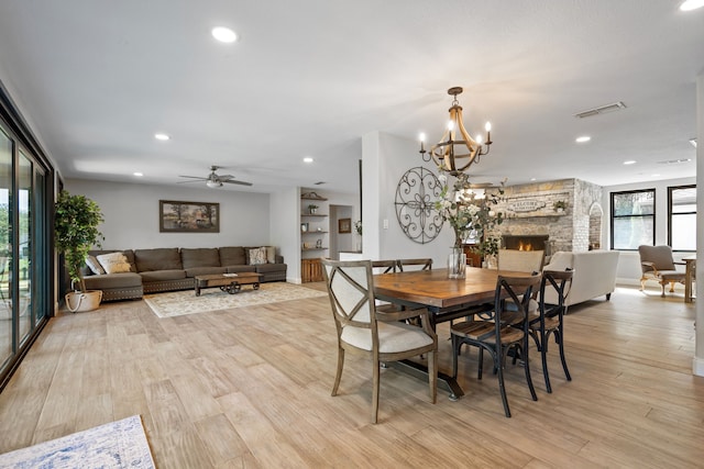 dining room with light wood-type flooring, ceiling fan with notable chandelier, and a fireplace